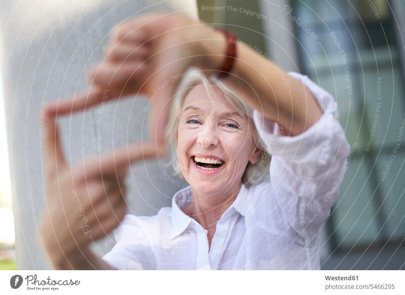 Porträt einer lachenden reifen Frau, die den Rahmen mit ihren Fingern formt freuen Glück glücklich sein glücklichsein Farben Farbtoene Farbton Farbtöne weiss