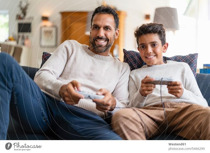 Glücklicher Vater und Sohn spielen Videospiel auf der Couch im Wohnzimmer (value=0) Leute Menschen People Person Personen Europäisch Kaukasier kaukasisch