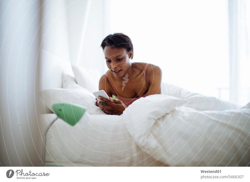 Frau liegt zu Hause im Bett und benutzt Mobiltelefon Leute Menschen People Person Personen Alleinstehende Alleinstehender Singles Unverheiratete Unverheirateter