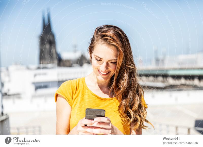 Deutschland, Köln, lächelnde Frau mit Mobiltelefon weiblich Frauen Smartphone iPhone Smartphones benutzen Erwachsener erwachsen Mensch Menschen Leute People