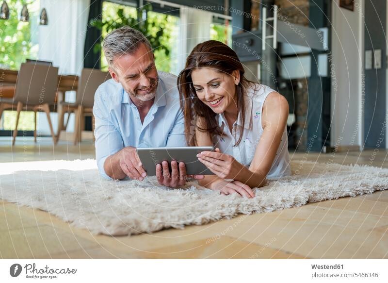 Glückliches Paar liegt zu Hause auf einem Teppich und teilt sich eine Tablette Teilen Sharing Zuhause daheim liegen liegend Tablet Computer Tablet-PC Tablet PC