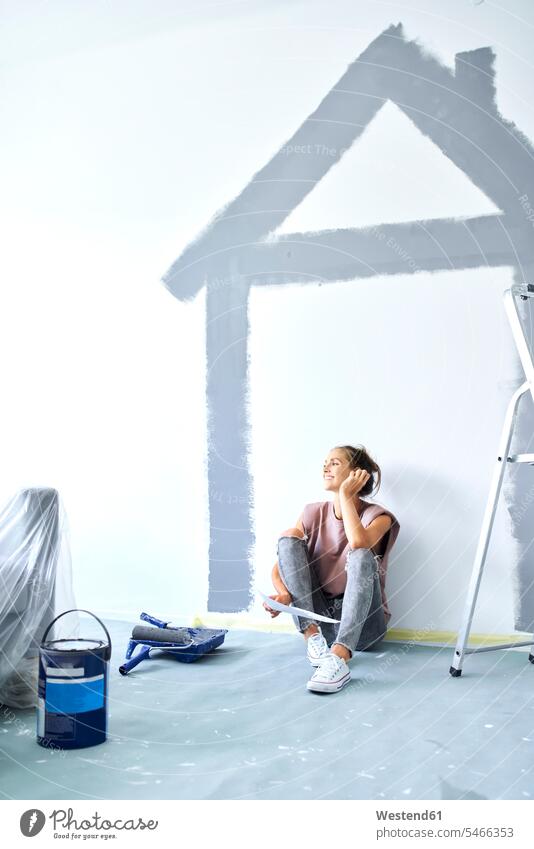 Junge Frau hält Papier in der Hand, während sie zu Hause gegen ein an die Wand gemaltes Haus sitzt Farbaufnahme Farbe Farbfoto Farbphoto Innenaufnahme