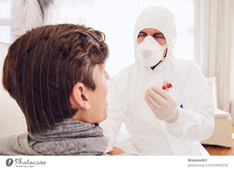 Arzt im Schutzanzug führt Coronavirus-Test an jungem Mann zu Hause durch Farbaufnahme Farbe Farbfoto Farbphoto Deutschland Innenaufnahme Innenaufnahmen innen