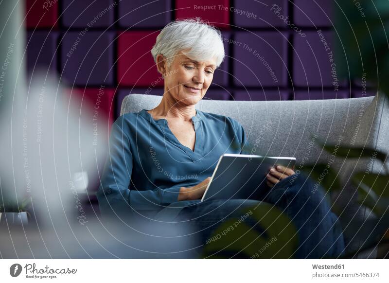Porträt einer älteren Geschäftsfrau, die auf einem Lounge-Stuhl sitzt und ein digitales Tablet benutzt geschäftlich Geschäftsleben Geschäftswelt Geschäftsperson