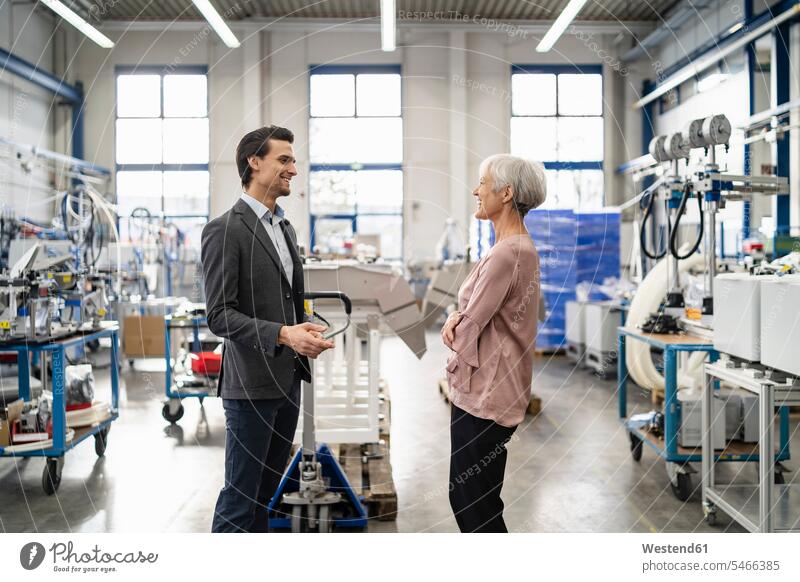 Lächelnder Geschäftsmann und ältere Geschäftsfrau im Gespräch in einer Fabrik sprechen reden Fabriken Businessmann Businessmänner Geschäftsmänner