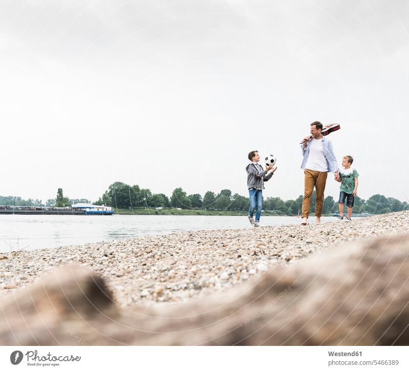 Glücklicher Vater mit zwei Söhnen und Fussball am Flussufer Sohn glücklich glücklich sein glücklichsein Fluesse Fluß Flüsse Fußball Fußbälle gehen gehend geht