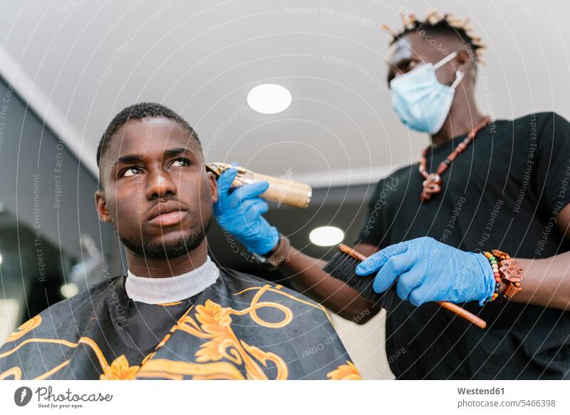Friseur trägt Maske und Handschuhe, während er den Kunden im Salon die Haare mit einem Rasiermesser schneidet Farbaufnahme Farbe Farbfoto Farbphoto Spanien