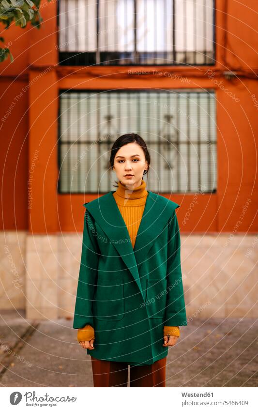 Junge Frau in grüner Jacke steht gegen Gebäude in der Stadt Farbaufnahme Farbe Farbfoto Farbphoto Spanien Freizeitkleidung Freizeitbekleidung casual