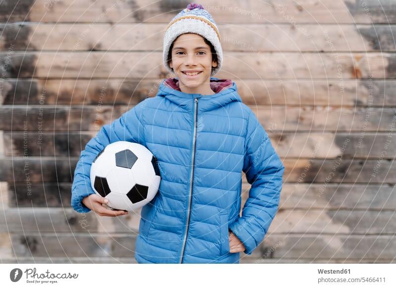 Lächelnder Junge in warmer Kleidung, der den Fussball an der Wand hält Farbaufnahme Farbe Farbfoto Farbphoto Spanien Freizeitbeschäftigung Muße Zeit Zeit haben