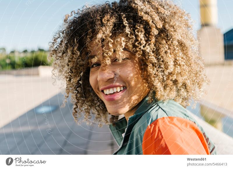 Glückliche junge Frau mit lockigem Haar an einem sonnigen Tag Farbaufnahme Farbe Farbfoto Farbphoto Außenaufnahme außen draußen im Freien Tageslichtaufnahme