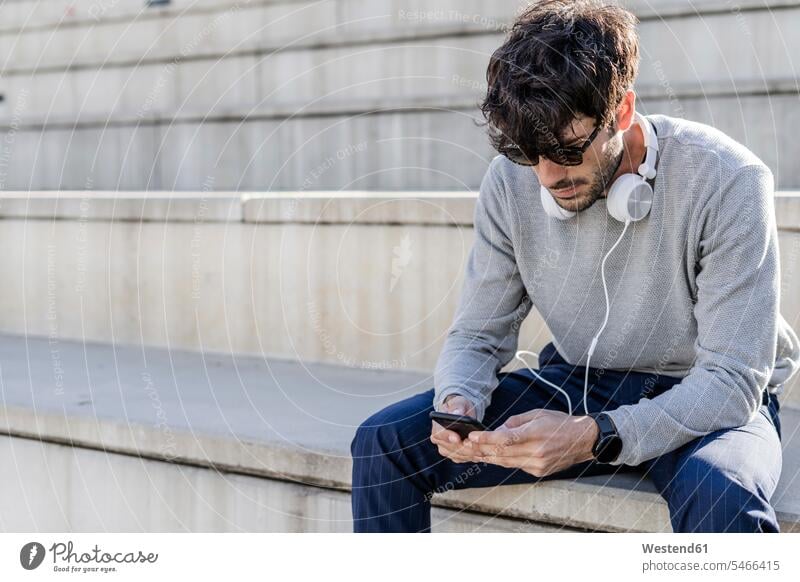 Mann sitzt auf einer Außentreppe und benutzt ein Smartphone Leute Menschen People Person Personen Europäisch Kaukasier kaukasisch 1 Ein ein Mensch