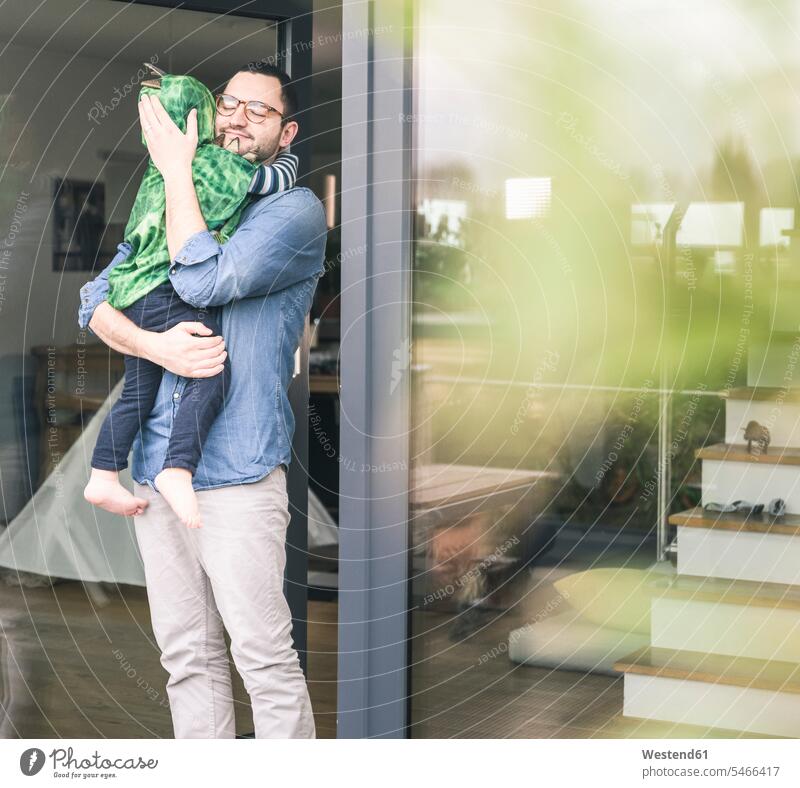 Liebevoller Vater trägt Sohn in einem Kostüm an der Terrassentür zu Hause tragen transportieren Terrassentuer Maskenkostüm Maskenkostüme Verkleidung Kostüme