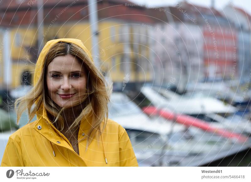 Dänemark, Kopenhagen, Porträt einer lächelnden Frau am Stadthafen bei regnerischem Wetter staedtisch städtisch Regenwetter Hafen Haefen Häfen weiblich Frauen
