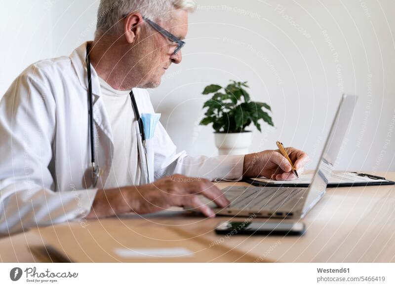 Leitender Arzt arbeitet am Laptop, während er in seiner Klinik sitzt Farbaufnahme Farbe Farbfoto Farbphoto Innenaufnahme Innenaufnahmen innen drinnen Tag