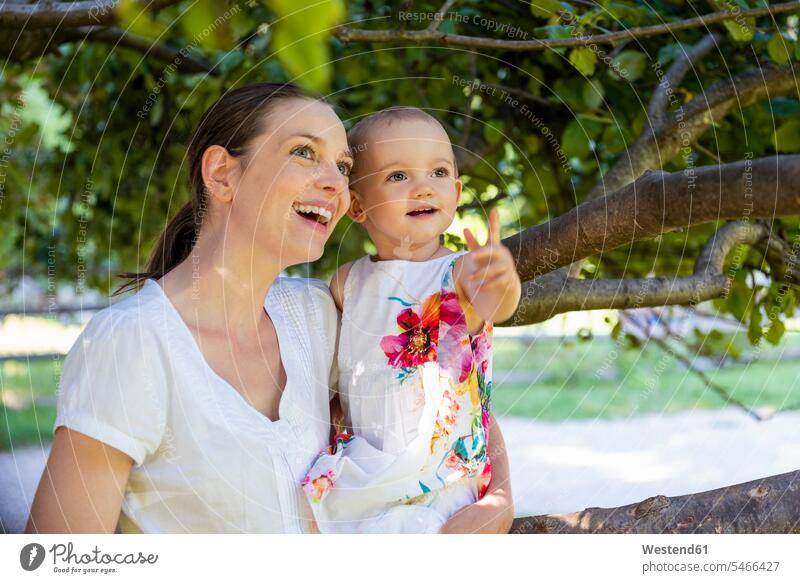 Glückliche Mutter und kleine Tochter unter einem Baum, die etwas entdecken Mamas Mami Mutti Mütter Muetter Mamis Muttis glücklich glücklich sein glücklichsein
