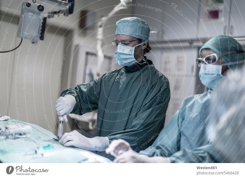 Neuroradiologe mit Assistent mit Spritze während einer Operation Assistentin OP Operationen operieren Chirurgie Operationskittel Krankenhaus Kliniken
