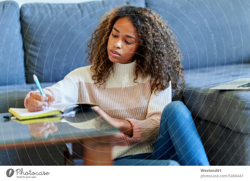 Afro junge Frau mit Laptop schreiben in Notizblock zu Hause Farbaufnahme Farbe Farbfoto Farbphoto Innenaufnahme Innenaufnahmen innen drinnen