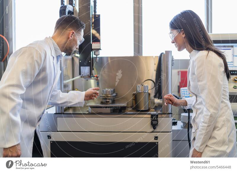 Kollegen in Laborkitteln und mit Schutzbrillen betrachten eine Maschine in einer modernen Fabrik Arbeitskollegen Fabriken ansehen Brille Maschinen schauen