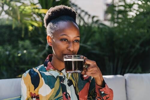 Porträt einer jungen Frau, die im Garten schwarzen Kaffee trinkt Gläser Trinkglas Trinkgläser Kleider Couch Couches Liege Sofas entspannen relaxen Jahreszeiten