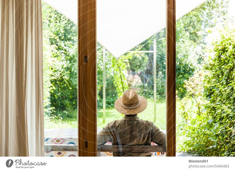Rückenansicht eines älteren Mannes mit Strohhut auf der Terrasse, der seinen Garten genießt Deutschland Lebensabend Auszeit Alles hinter sich lassen abschalten