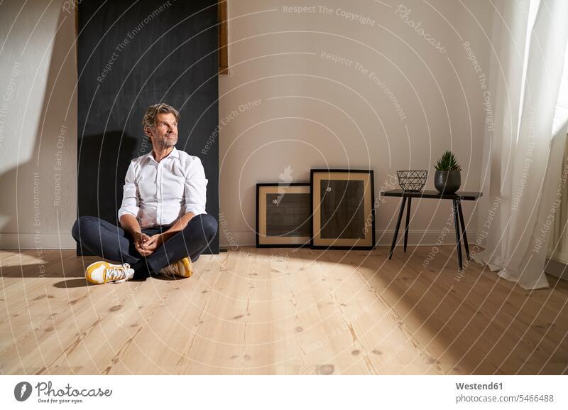 Porträt eines entspannten reifen Mannes, der zu Hause auf dem Boden sitzt und in die Ferne schaut Rahmen Hemden Farben Farbtoene Farbton Farbtöne weiss weiße