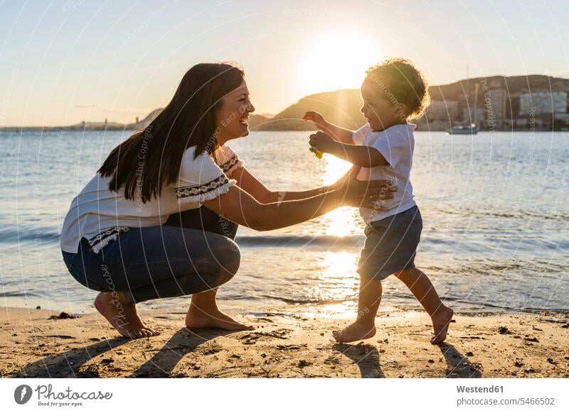 Fröhliche Mutter spielt mit Sohn bei Sonnenuntergang am Strand Farbaufnahme Farbe Farbfoto Farbphoto Spanien Freizeitbeschäftigung Muße Zeit Zeit haben