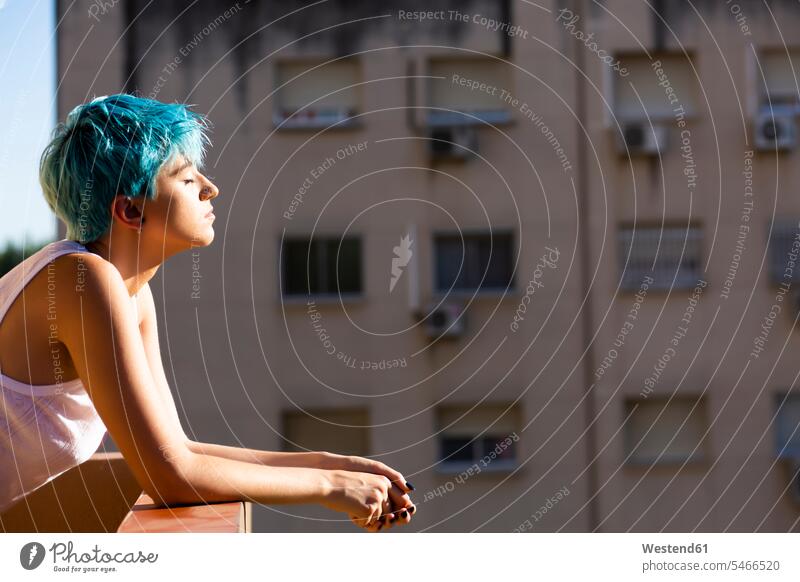 Androgyne junge Frau mit blauen Haaren genießt Sonnenlicht auf dem Balkon Leute Menschen People Person Personen Europäisch Kaukasier kaukasisch 1 Ein ein Mensch