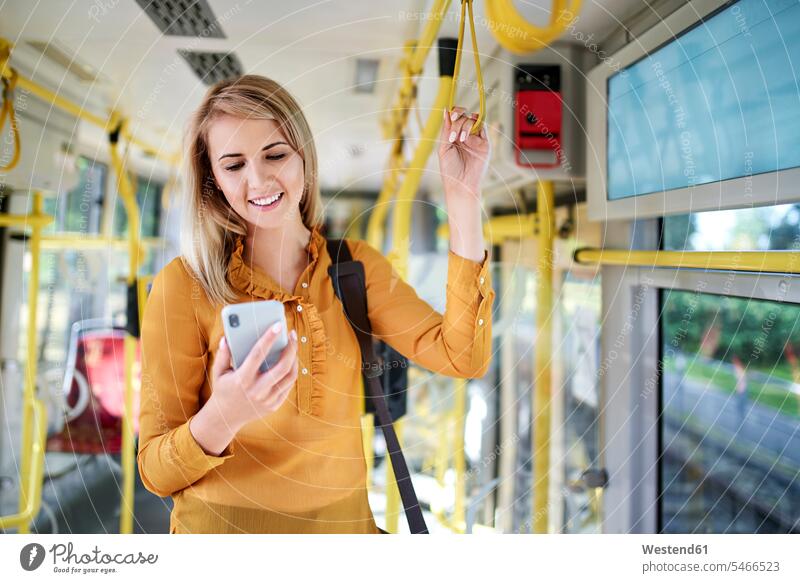 Lächelnde junge Frau mit Smartphone in der Straßenbahn Leute Menschen People Person Personen Europäisch Kaukasier kaukasisch 1 Ein ein Mensch eine