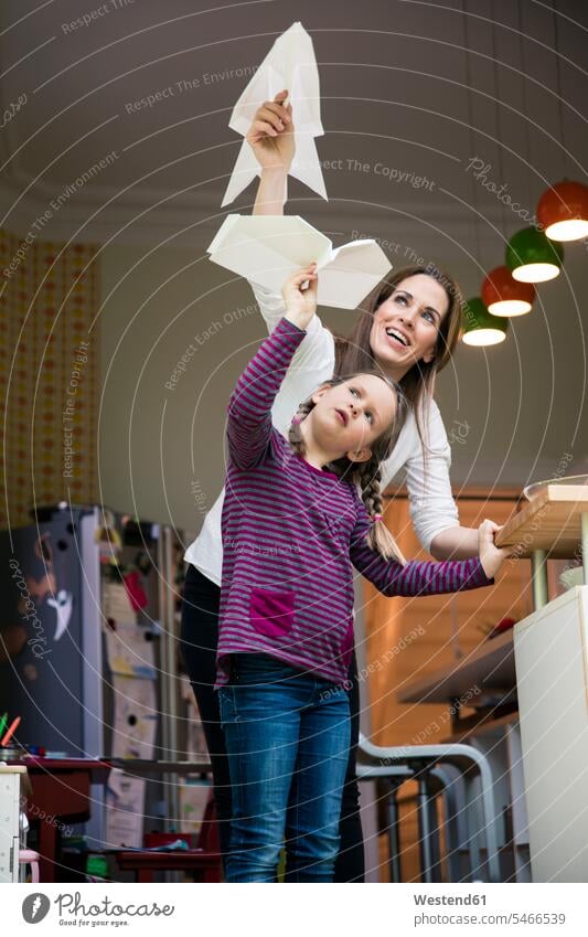 Glückliche Mutter und Tochter werfen zu Hause gemeinsam ein Papierflugzeug Wurf Zuhause daheim Gemeinsam Zusammen Miteinander Mami Mutti Mütter Mama