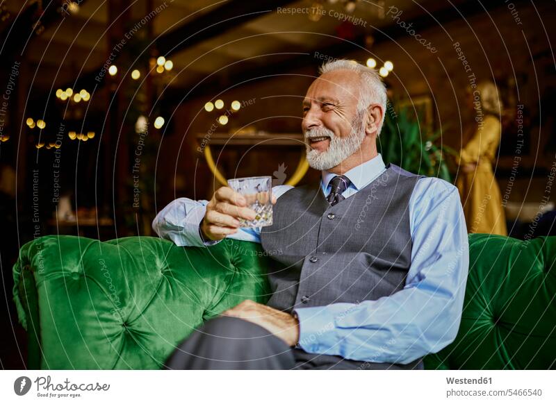 Porträt eines eleganten älteren Mannes, der auf einer Couch in einer Bar sitzt und einen Becher hält Portrait Porträts Portraits Sofa Couches Liege Sofas Männer
