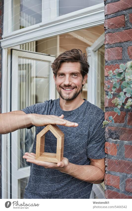 Porträt eines lächelnden Mannes am Hauseingang, der ein Hausmodell hält Häuser Haeuser Portrait Porträts Portraits Modell Modelle halten Männer männlich Gebäude