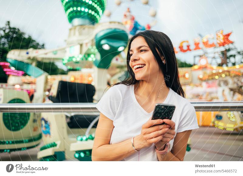 Fröhliche junge Frau hält Smartphone in der Hand und schaut weg auf Vergnügungspark Farbaufnahme Farbe Farbfoto Farbphoto Ukraine Freizeitbeschäftigung Muße