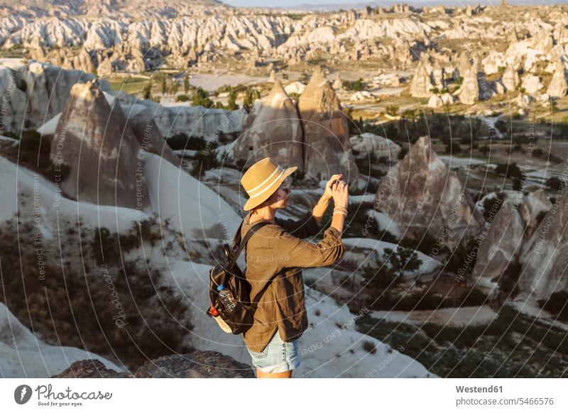 Seitenansicht einer jungen Frau beim Fotografieren von Felsformationen mit dem Smartphone in Goreme, Kappadokien, Türkei Abenteuer abenteuerlich Rucksack