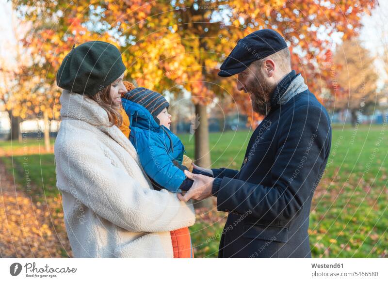 Glückliches, liebevolles Paar mit kleinem Sohn im Park Jacken Mützen freuen Frohsinn Fröhlichkeit Heiterkeit behüten behütet geborgen Sicherheit geniessen