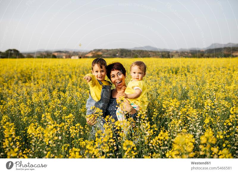 Spanien, Porträt einer lachenden Mutter mit kleinem Sohn und Tochter in einem Rapsfeld Portrait Porträts Portraits Söhne Töchter Mami Mutti Mütter Mama