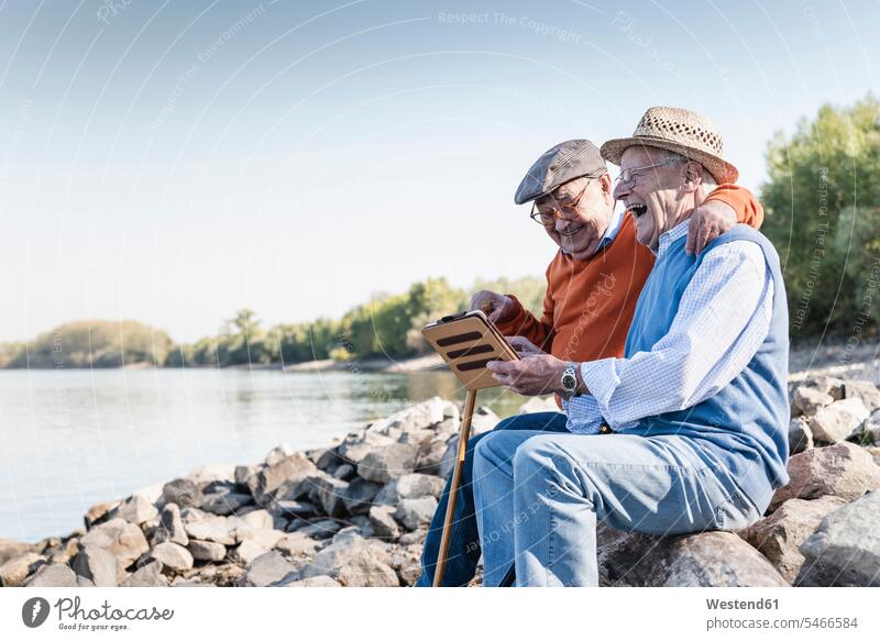 Zwei alte Freunde sitzen am Flussufer und benutzen ein digitales Tablet sitzend sitzt benützen Beste Freunde Bester Freund Tablet Computer Tablet-PC Tablet PC