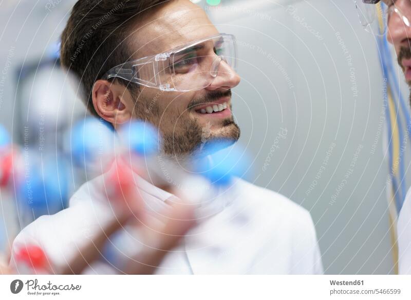 Lächelnder männlicher Wissenschaftler, der die Molekularstruktur hält, während er einen Kollegen im beleuchteten Labor ansieht Farbaufnahme Farbe Farbfoto