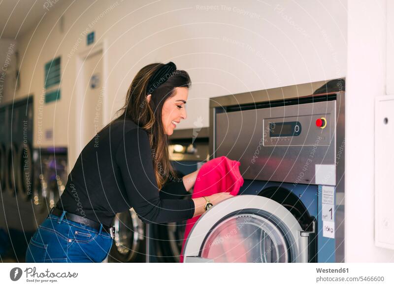 Junge Frau, die in einem Waschsalon die Wäsche wäscht Leute Menschen People Person Personen Europäisch Kaukasier kaukasisch 1 Ein ein Mensch nur eine Person