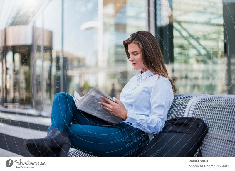 Porträt einer jungen Geschäftsfrau, die auf einer Bank sitzt und Zeitung liest Geschäftsfrauen Businesswomen Businessfrauen Businesswoman Zeitungen lesen