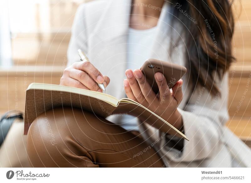 Nahaufnahme einer Frau, die mit einem Smartphone auf einer Treppe sitzt und sich Notizen macht Informationen Hosen Lederhosen Stifte Telekommunikation