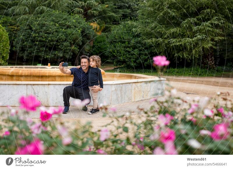 Glücklicher Vater und Sohn bei der Aufnahme eines Selfies im Park glücklich glücklich sein glücklichsein Parkanlagen Parks Papas Väter Vati Vatis Papis Söhne