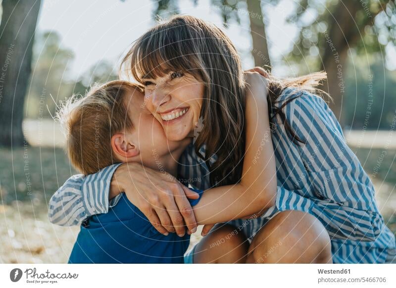 Lächelnde Mutter umarmt Sohn im öffentlichen Park Farbaufnahme Farbe Farbfoto Farbphoto Außenaufnahme außen draußen im Freien Tag Tageslichtaufnahme