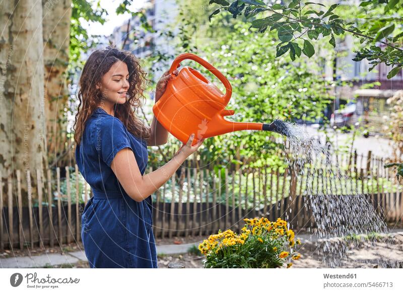 Junge Frau gießt Blumen im Garten Zäune Jahreszeiten sommerlich Sommerzeit freuen Glück glücklich sein glücklichsein zufrieden Gartenarbeit Gartenbau Muße