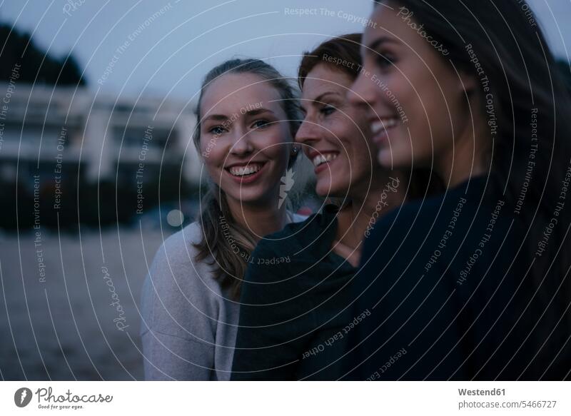 Deutschland, Hamburg, glückliche Mutter mit zwei Teenager-Mädchen am Strand am Elbufer am Abend Glück glücklich sein glücklichsein Teenagerin junges Mädchen