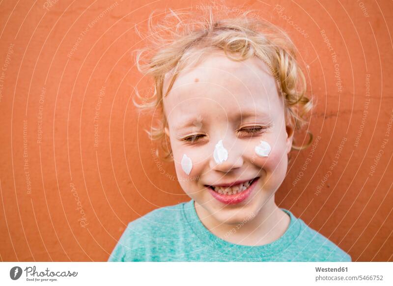 Porträt eines lächelnden kleinen Jungen mit drei Cremeklecksen im Gesicht T-Shirts Cremes Sonnenmilch Jahreszeiten sommerlich Sommerzeit freuen zufrieden Farben