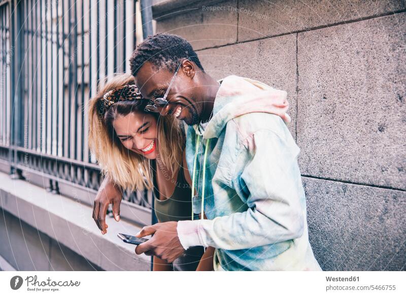 Lachendes Paar benutzt Mobiltelefon im Freien Leute Menschen People Person Personen Afrikanisch Afrikanische Abstammung dunkelhäutig Farbige Farbiger Schwarze