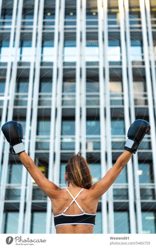 Sportliche junge Frau mit Boxhandschuhen in der Stadt hebt die Arme sportlich staedtisch städtisch boxen weiblich Frauen Boxen Boxsport Boxkampf Boxkaempfe