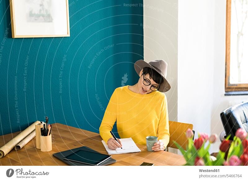 Geschäftsfrau im Büro zu Hause schreiben auf ein Stück Papier hält Kaffeebecher Zuhause daheim Frau weiblich Frauen aufschreiben notieren schreibend Schrift