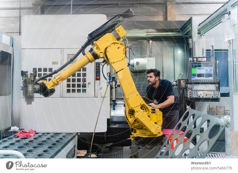 Junger männlicher Arbeiter analysiert Roboterarm in Fabrik Farbaufnahme Farbe Farbfoto Farbphoto Innenaufnahme Innenaufnahmen innen drinnen Österreich Beruf