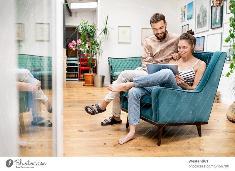 Junges Paar sitzt im Sessel und benutzt ein digitales Tablett Leute Menschen People Person Personen Europäisch Kaukasier kaukasisch 2 2 Menschen 2 Personen zwei